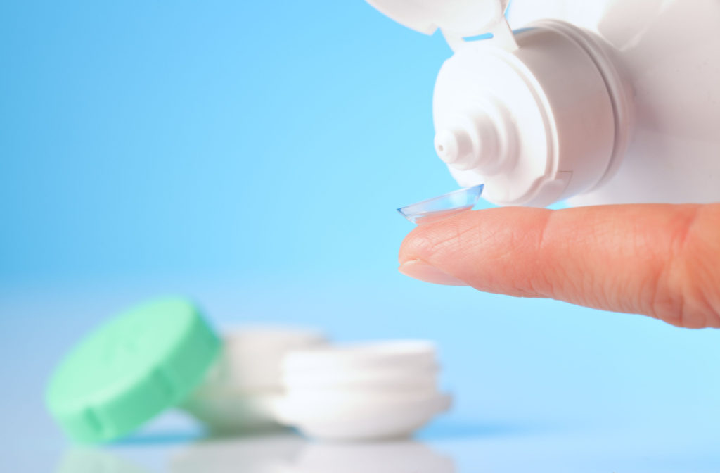 Contact lens solution being poured onto a contact lens on a fingertip with a contact lens case sitting in the background.