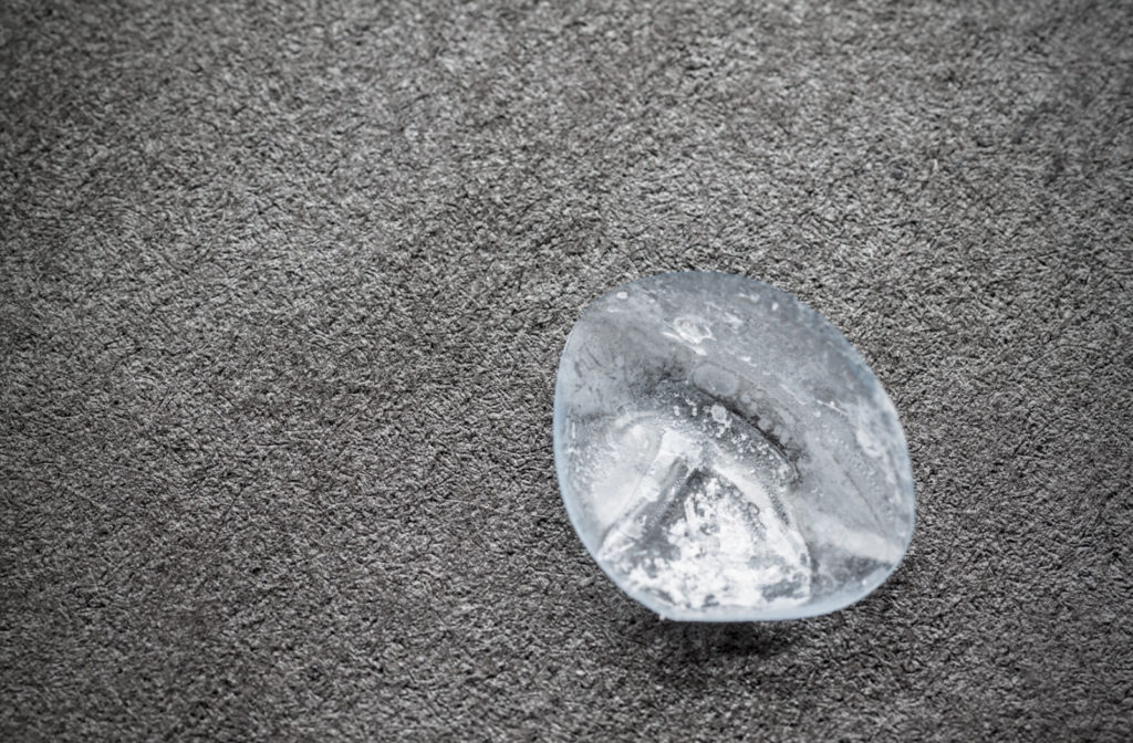 A dry and damaged contact lens sitting on a gray surface.