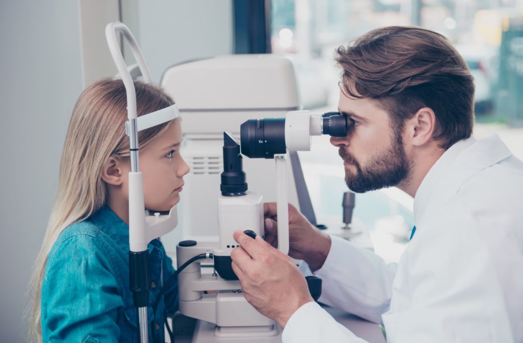 A male optometrist using a medical device to examine the eyes of a child patient and look for potential eye problems.