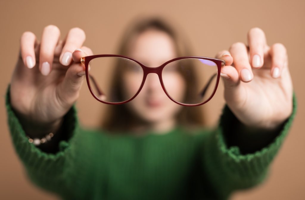 Woman holding a pair of red glasses in focus with her face blurred in the background, illustrating voluntary control over vision focus.