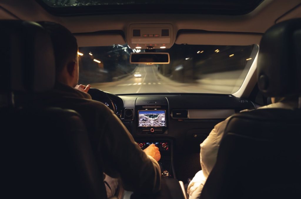 Looking out the front window of a car as a couple drives at night.