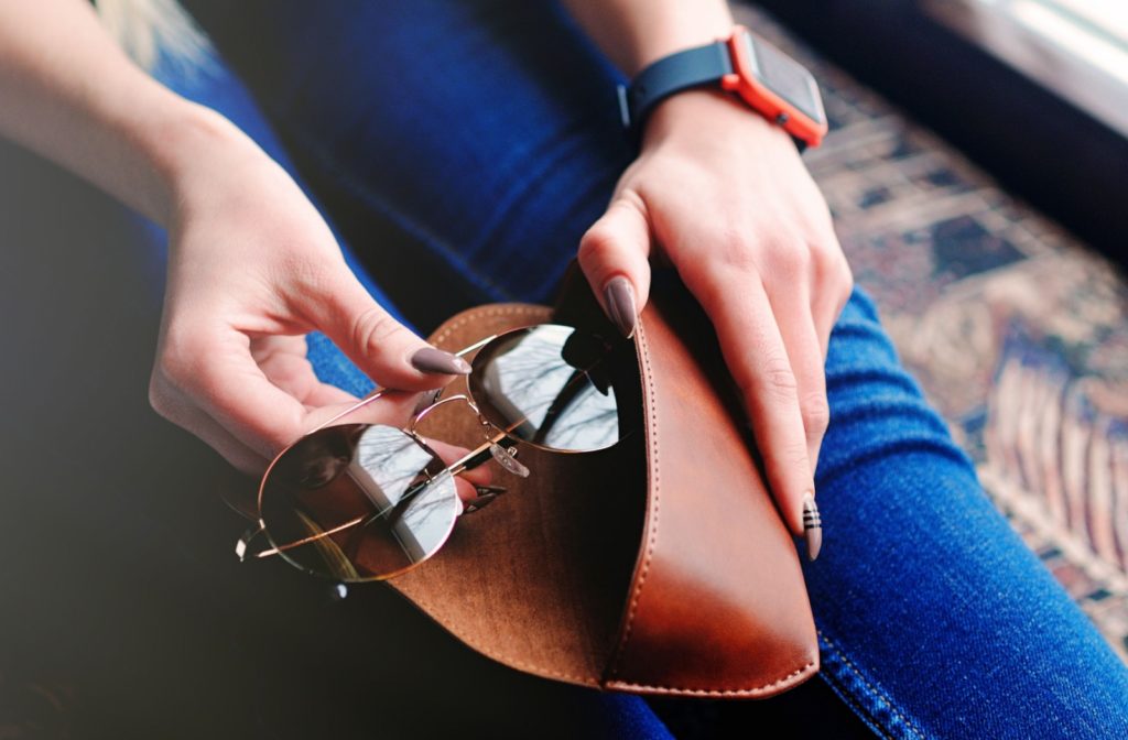 Person placing sunglasses into a brown leather case, focusing on proper storage.