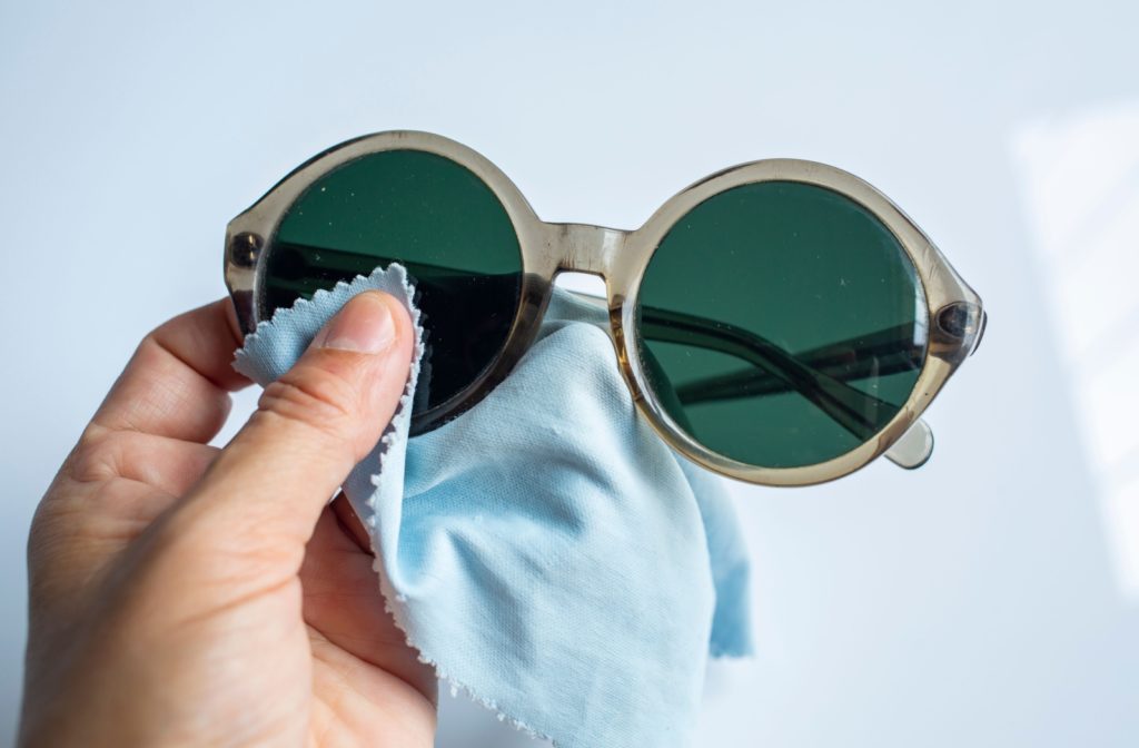 Hand cleaning sunglasses with a microfiber cloth to maintain lens clarity.