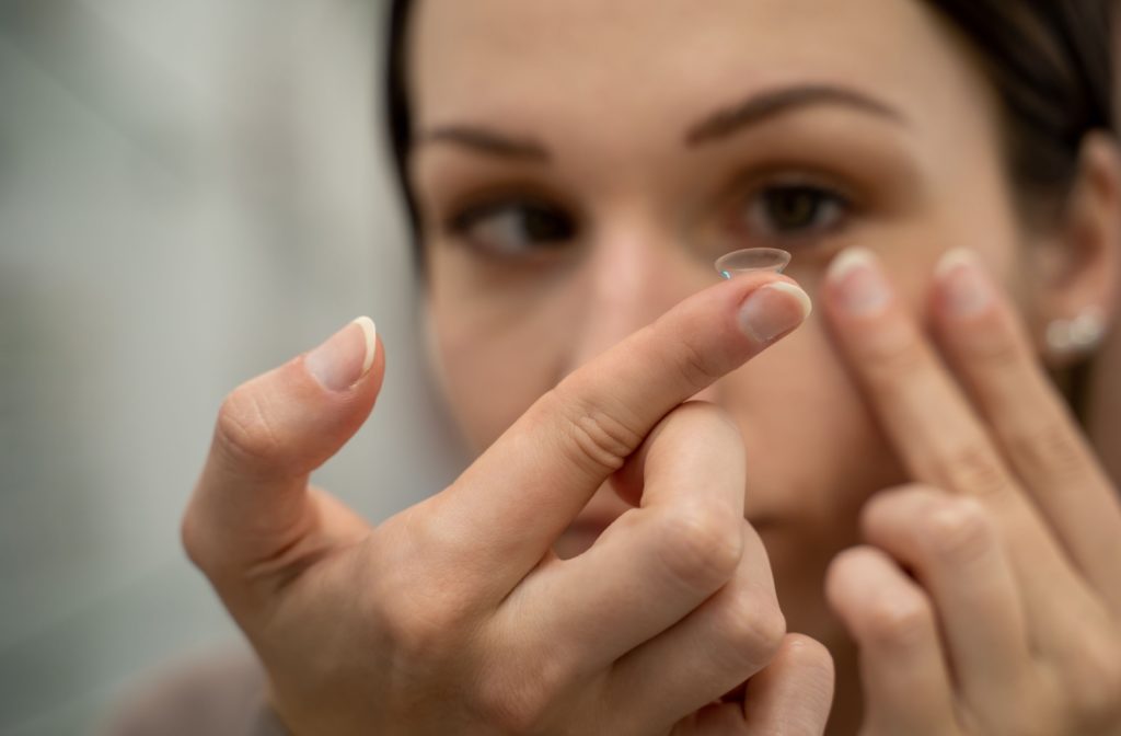 A person holds a contact lens up on their finger in front of their face while preparing to put it in their eye for the day.