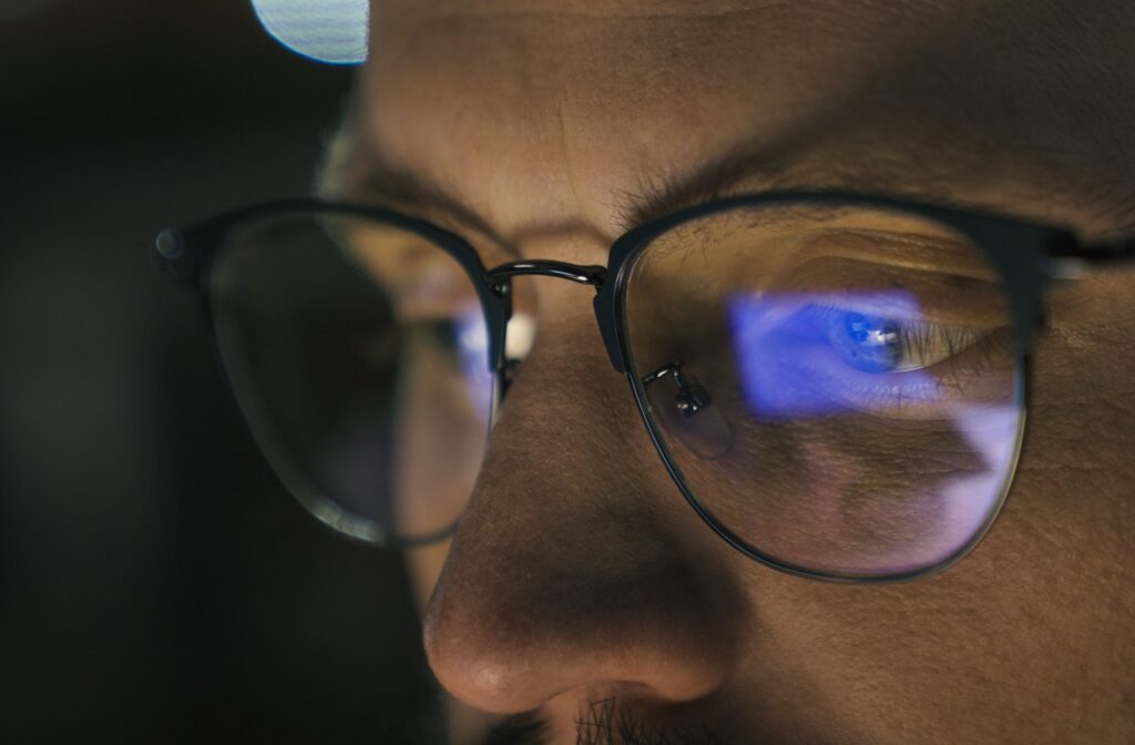 A close-up image of a young professional's blue light glasses while they work late at night.