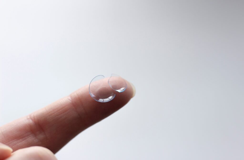 A close-up of a finger holding a torn, soft contact lens.