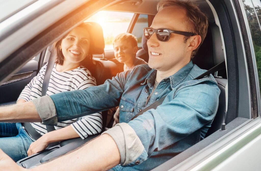 A person drives with polarized sunglasses on while two passengers smile beside and behind them.