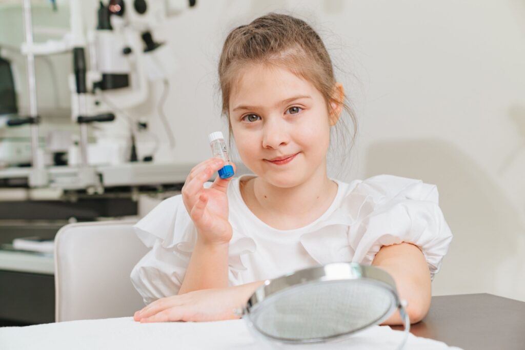 A child at their optometrist's office, holding up contact lenses for myopia control.